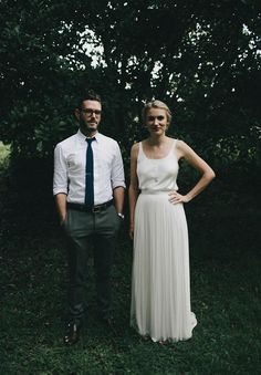 a man and woman standing next to each other in front of some green grass with trees behind them