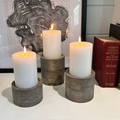 three white candles sitting on top of a table next to books and a framed photograph