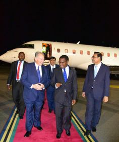 two men in suits and ties walking down a red carpet next to a white plane