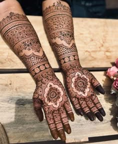 two hands with henna tattoos on them, one is showing the intricate design and the other has flowers