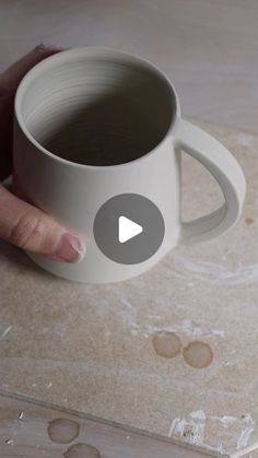 a person holding a white coffee cup on top of a wooden table with holes in it