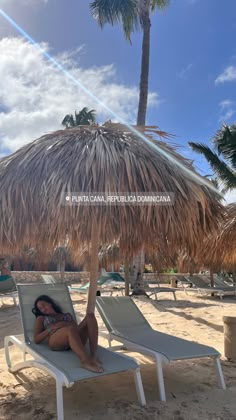 a woman laying on top of a lawn chair under an umbrella next to palm trees