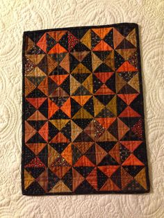 an orange and black quilted wall hanging on a white bedding with decorative patterns