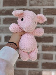 a hand holding a pink teddy bear in front of a brick wall