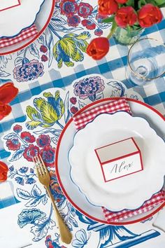 a place setting with red and white plates, silverware and flowers on the table