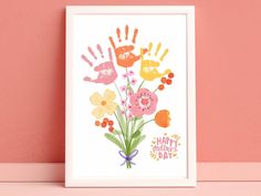 an art print with flowers and hand prints on the front, against a pink wall