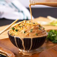 someone pouring sauce into a bowl filled with food on top of a wooden cutting board