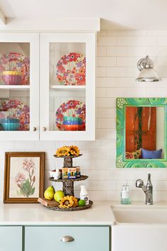 a kitchen with white cabinets and colorful plates on the shelves above the sink is decorated with flowers