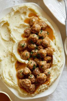 mashed potatoes with meatballs and gravy on a plate next to a fork