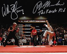 two men performing karate moves in front of an audience with autographs on the wall