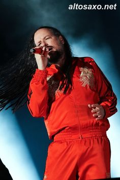 a man with long hair on stage holding a microphone in his hand and singing into the microphone