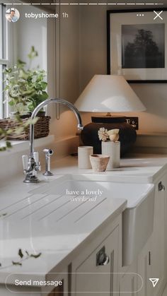 a white sink sitting under a window next to a lamp in a room with pictures on the wall