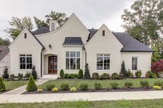 a large white house with lots of windows and bushes in front of the door is surrounded by greenery