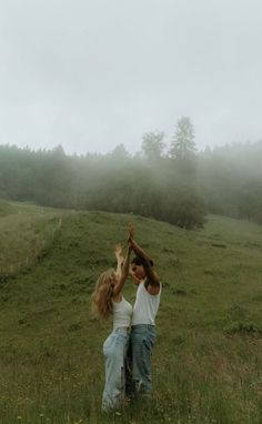 two people standing in a field reaching up into the sky with their hands together,