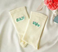 two white socks with green lettering on them sitting next to a pink carnation flower