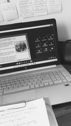 an open laptop computer sitting on top of a desk next to a pile of papers