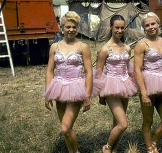 three young women in pink dresses standing next to each other on the grass near a train