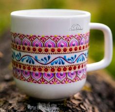 a white coffee cup sitting on top of a tree stump covered in colorful designs and beads