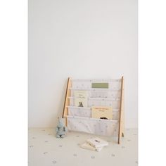 a book rack with books on it and a stuffed animal next to it in front of a white wall