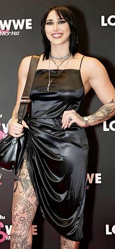 a woman in a black dress with tattoos on her arm and leg, posing for the camera