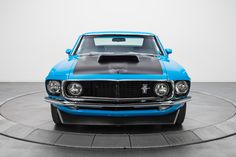 a blue mustang sitting on top of a black and white circular surface with the hood up