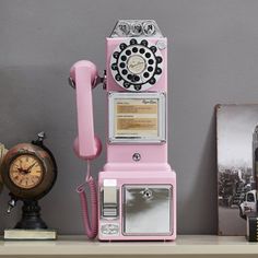 an old fashioned pink phone sitting on top of a shelf next to a clock and other items