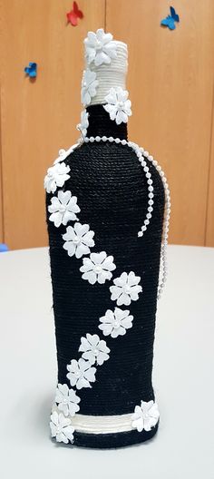 a black vase with white flowers and pearls on the top is sitting on a table