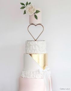 a three tiered wedding cake with a rose on top and a gold heart decoration