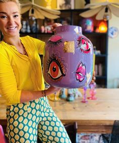 a woman holding up a vase with an eye painted on it's front and side