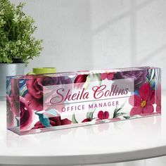 a clear box with flowers on it sitting on a table next to a potted plant