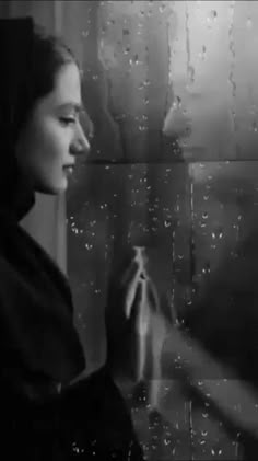 a woman standing in front of a window with rain drops on it