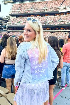 a woman wearing a jean jacket and fringe skirt at a concert with people in the stands