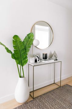 a plant in a white vase next to a mirror on a table with other items