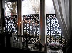 an open window with white curtains and candles on the windowsill, in front of a wrought iron fence