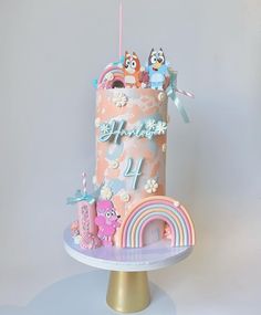 a pink birthday cake decorated with owls and rainbows is on a gold stand against a gray background