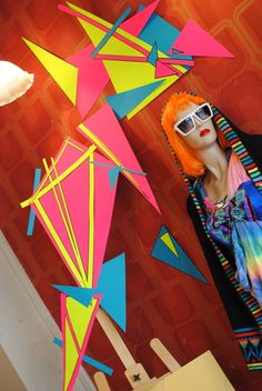 a mannequin wearing sunglasses and colorful clothing in front of a wall with paper art