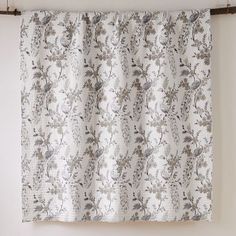 a curtain hanging on a wall in front of a window with white and gray flowers