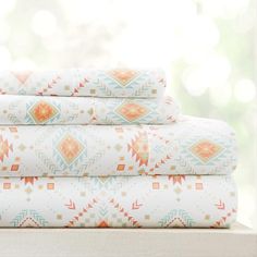 a stack of bed sheets with an orange and blue pattern on them in front of a window