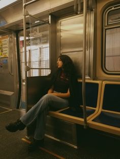 a woman sitting on a subway train seat with her legs crossed and looking out the window