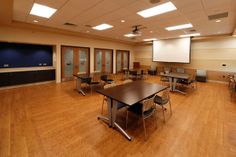 an empty classroom with tables and chairs in the center, on hard wood flooring