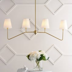 a vase with white flowers on top of a table next to a wall mounted lamp