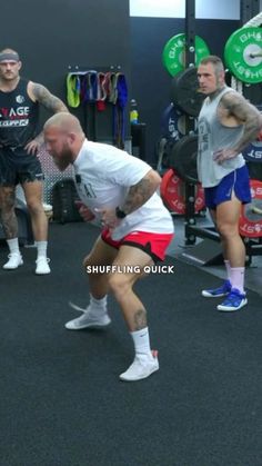 a group of men in a gym doing squats with one man holding a barbell