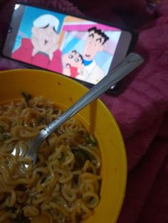 a yellow bowl filled with noodles next to a cell phone