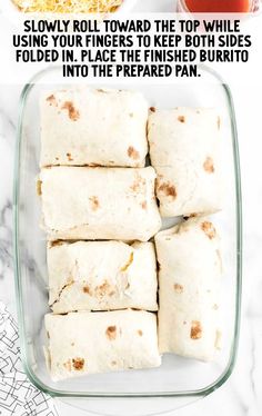 burritos in a glass baking dish on a marble counter top with text overlay that reads, slow roll toward the top while using your fingers to keep both sides folded in place