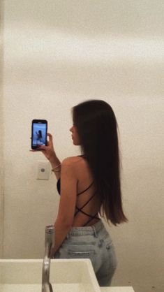 a woman standing in front of a bathroom mirror taking a selfie with her cell phone