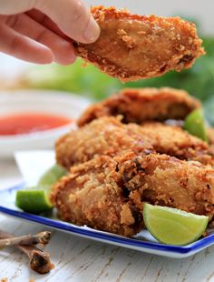 a person is picking up some fried food from a blue and white plate with lime wedges