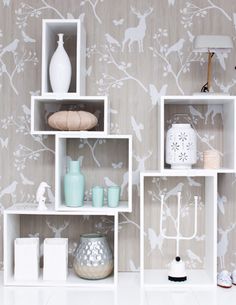 a shelf with vases, candles and other items on it in front of a wallpapered background