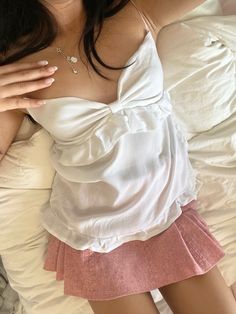 a woman laying on top of a bed wearing a white tank top and pink skirt