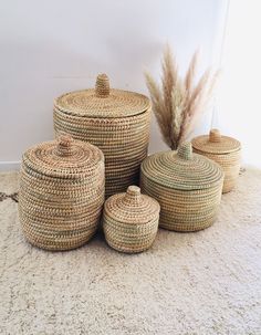 four woven baskets on the floor with some dried grass in front of them and a plant