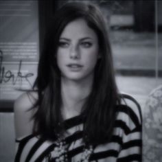 a black and white photo of a woman with long hair wearing a striped shirt looking at the camera